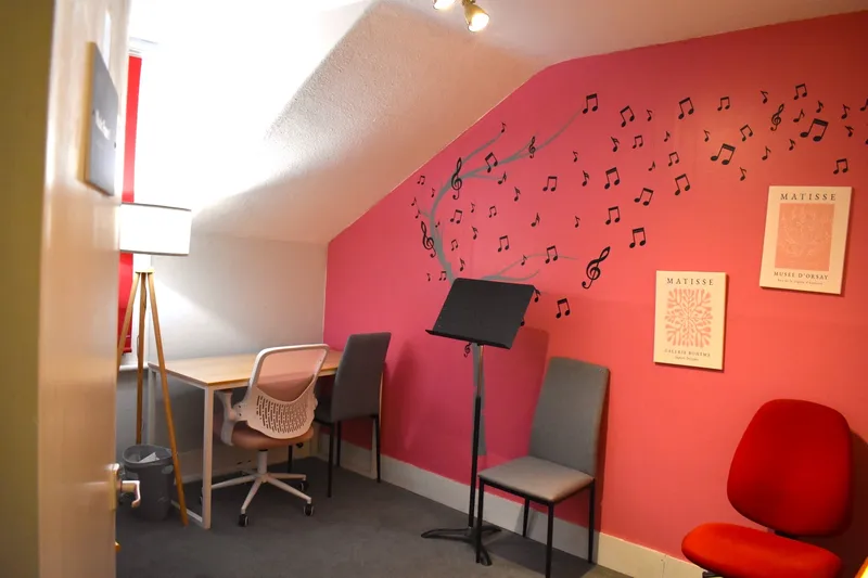 The teaching room at Bromley Conservatoire — a bright, private music room with an upright piano, music stands, and chairs arranged for one-to-one guitar lessons
